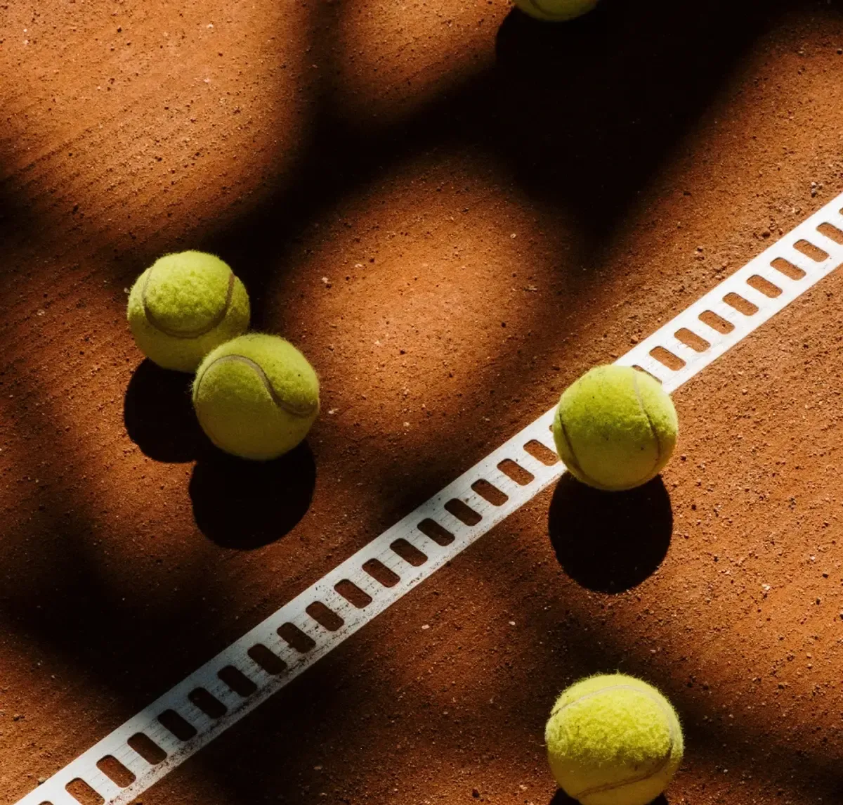 Noleggio racchetta e palline: palline da tennis appoggiate sulla linea di un campo in terra rossa