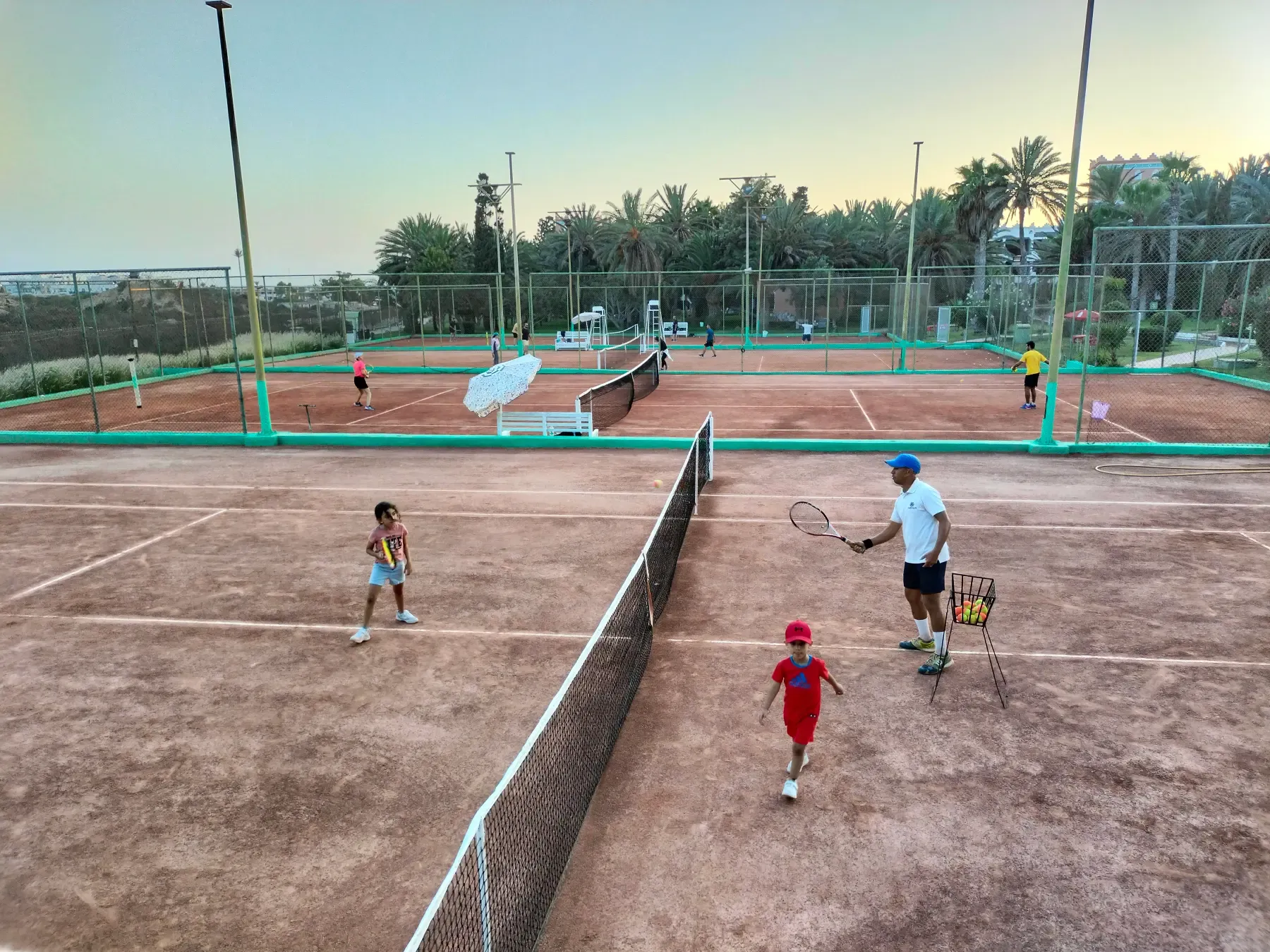 Il circolo di tennis nel cuore di Agadir: i suoi quattro campi in terra rossa al tramonto, un maestro e due bambini a rete