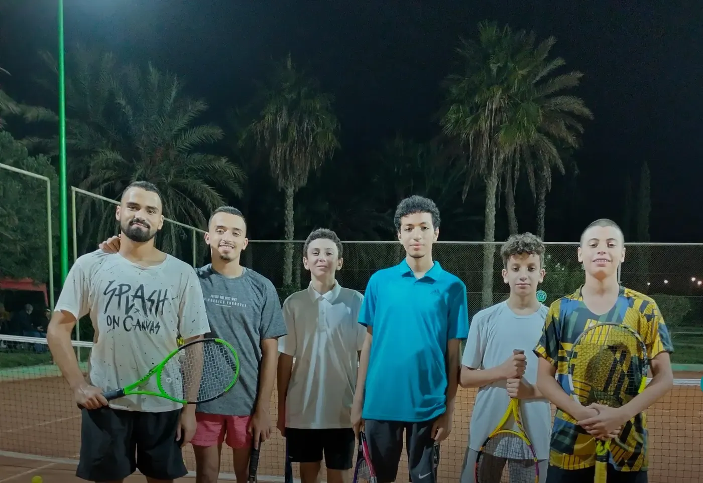 Die Gemeinschaft des Clubs: die Gruppe der Tennisschule unter Flutlicht auf dem Platz, Schläger in der Hand