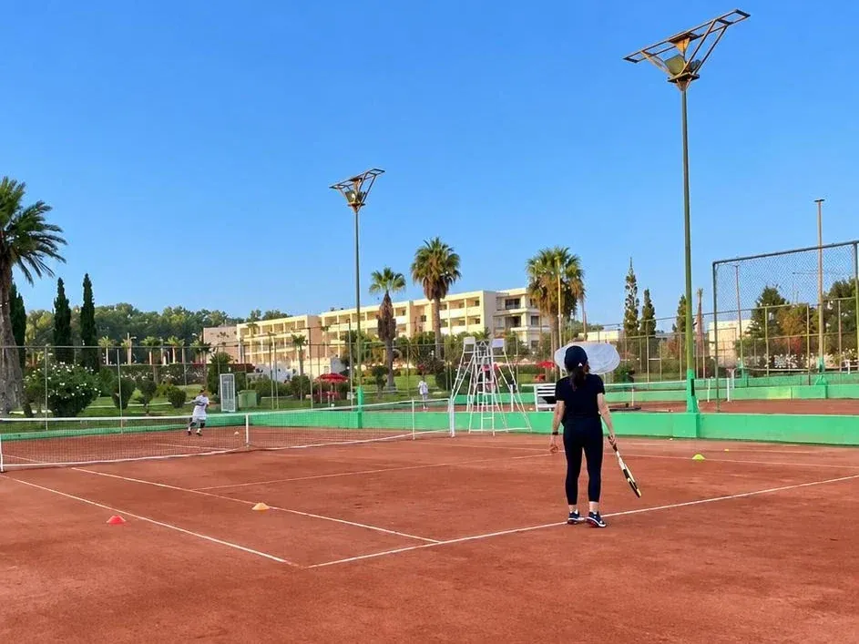 Tennisplatz mieten in Agadir: Sandplätze des Clubs bei Tag, umgeben von Palmen und Flutlichtmasten